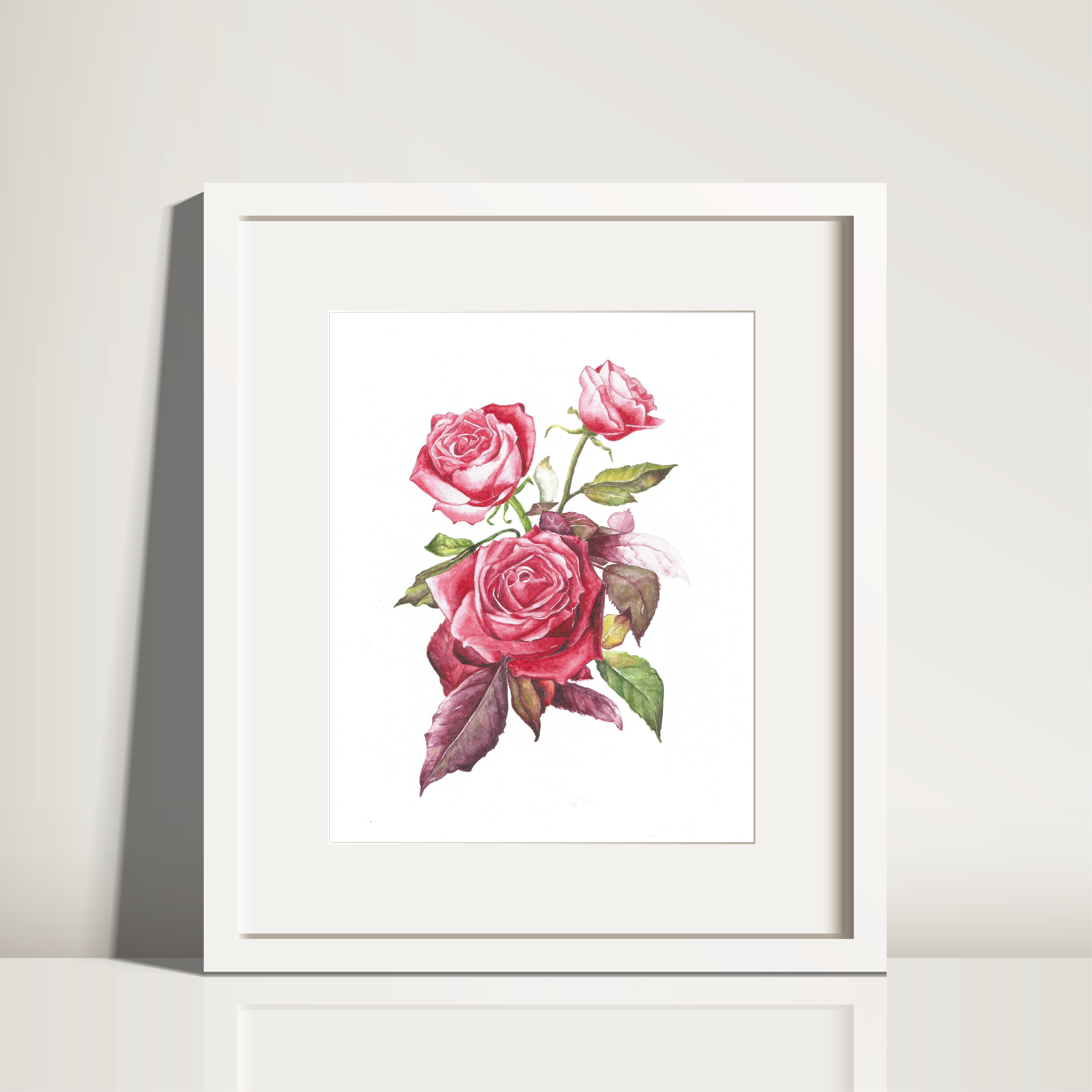 A framed and matted watercolor painting of pink roses displayed on a white surface.